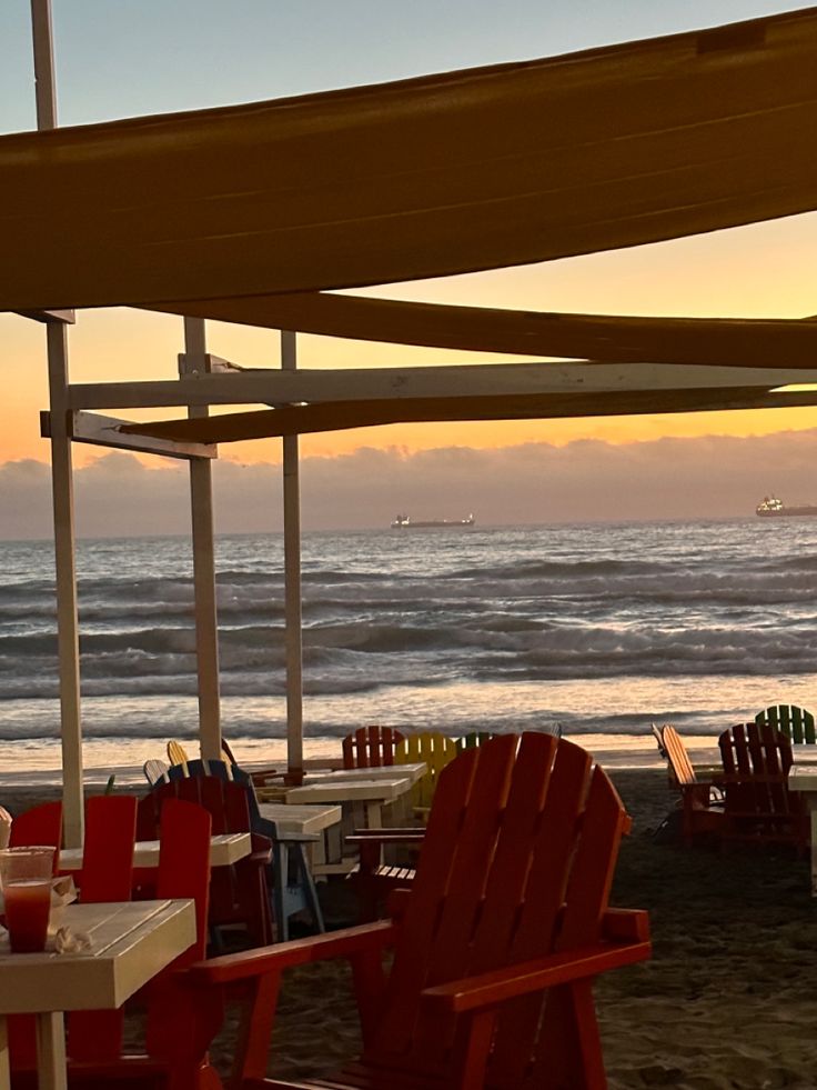 chairs and tables on the beach under an awning at sunset, with waves in the background