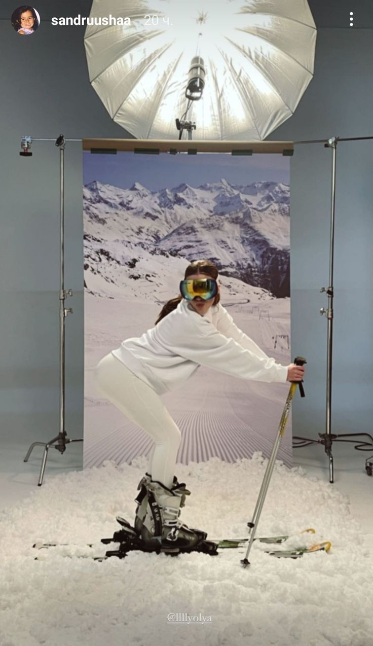 a woman standing in the snow with skis on her feet and an umbrella over her head