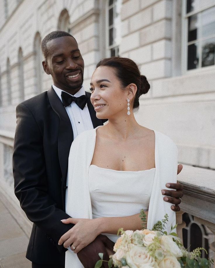 a bride and groom standing together in front of a building with flowers on the balcony