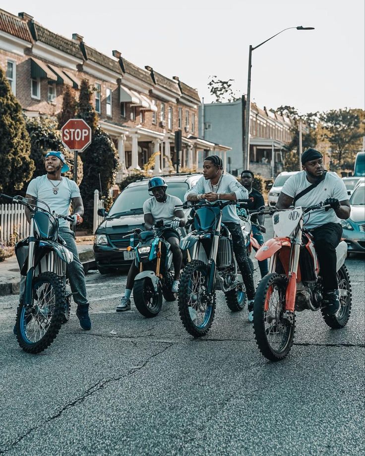 three men are riding motorcycles in the street with other people standing around them and cars parked on the side of the road