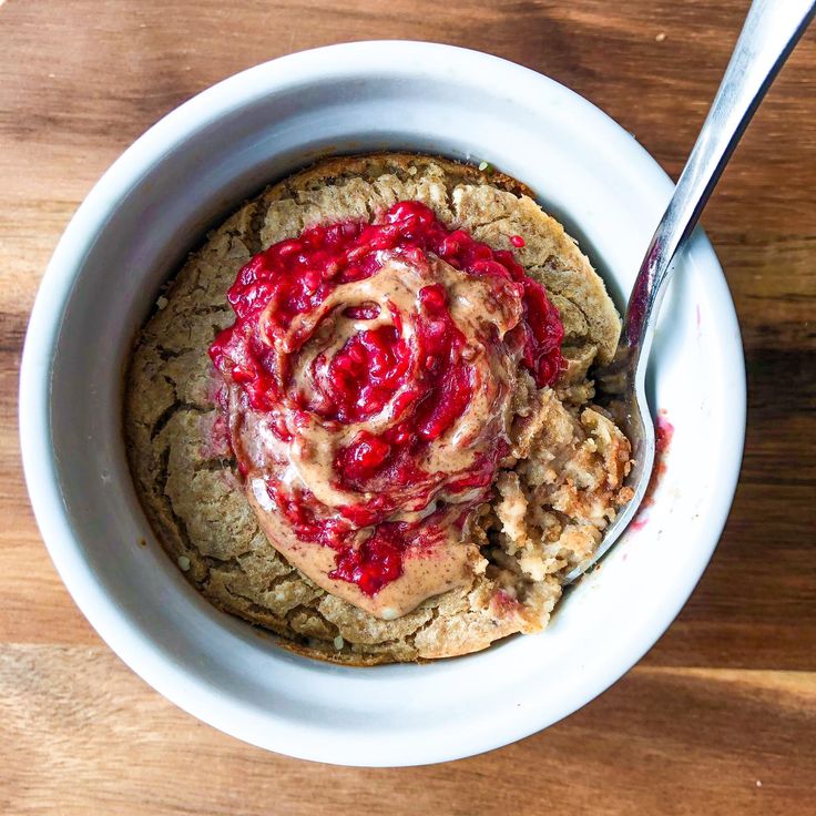 a white bowl filled with oatmeal and strawberry jam on top of a wooden table