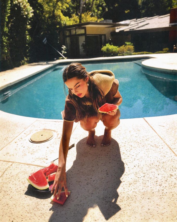 a woman bending over to pick up some watermelon by the swimming pool with her shoes on