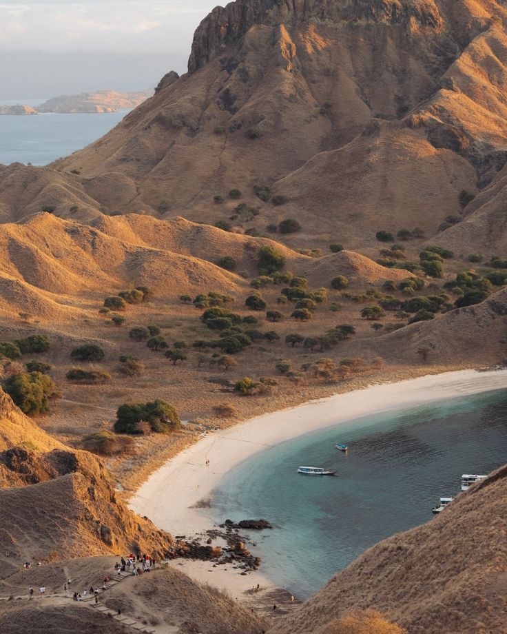 the beach is surrounded by mountains and blue water with boats in the water on it