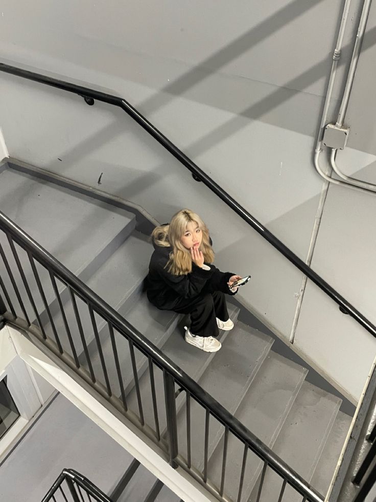 a woman sitting on top of a set of stairs holding a cell phone in her hand