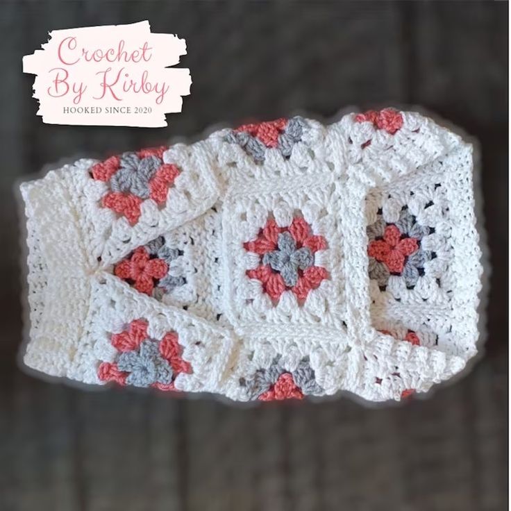 a crocheted baby blanket with red and gray flowers on the front, sitting on top of a wooden surface