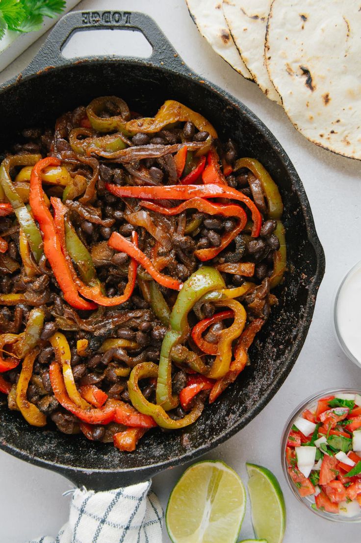 a skillet filled with black beans and peppers next to tortilla chips on a white table