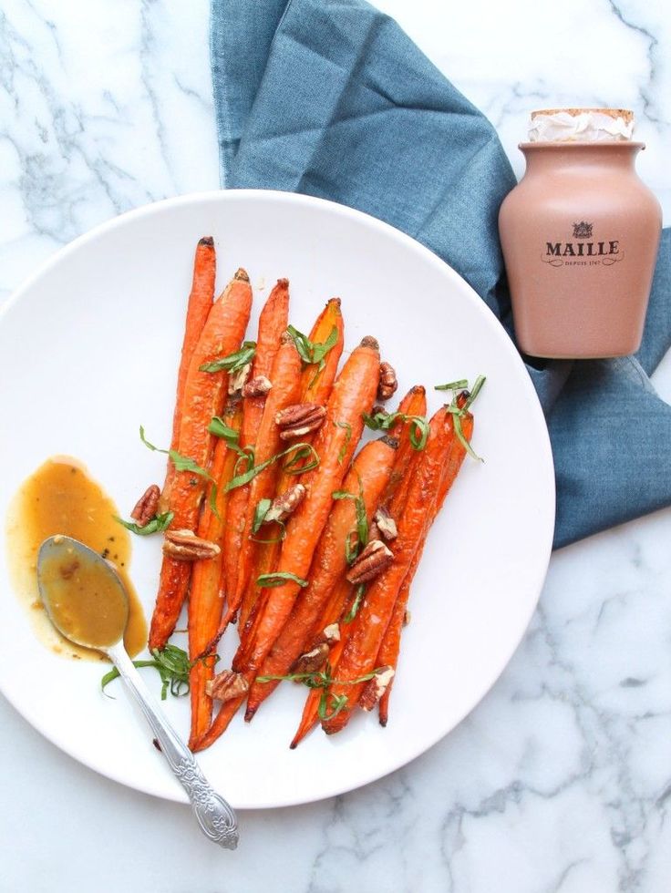 a white plate topped with sliced carrots next to a jar of mustard