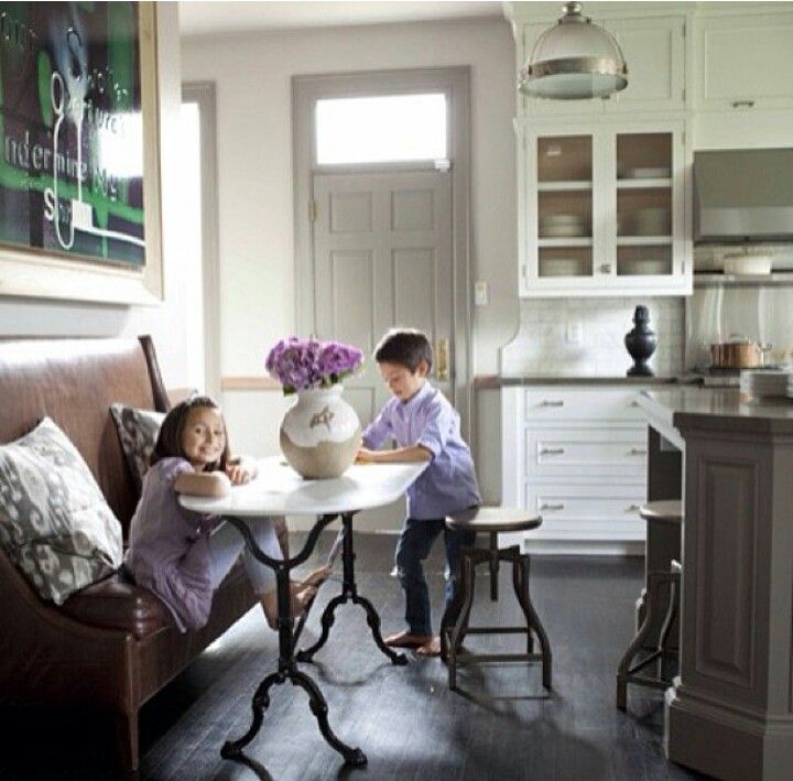 two children sitting at a table in a kitchen with white cabinets and gray flooring