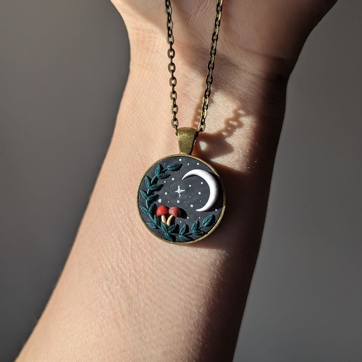 a woman's hand holding a necklace with an image of the moon and stars on it