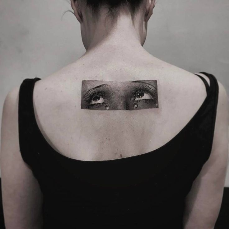 a woman's back shoulder with an eye tattoo on it