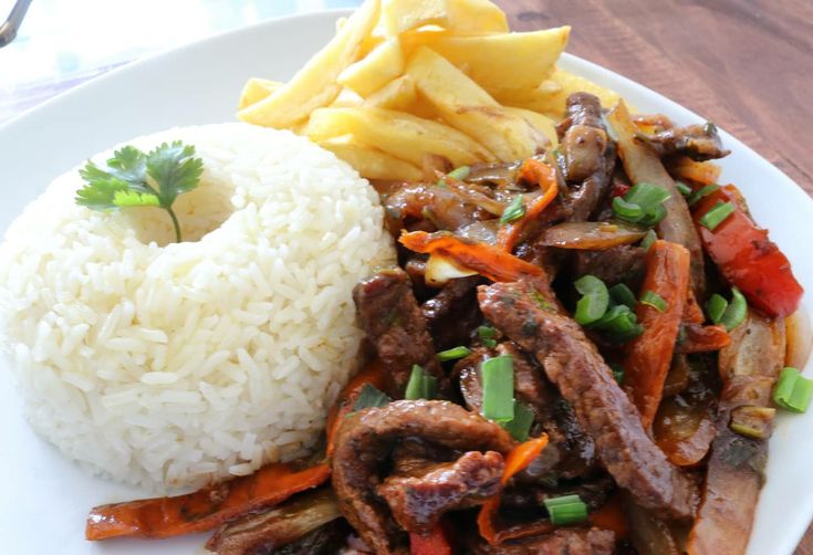 a white plate topped with meat, rice and veggies next to a pile of fries