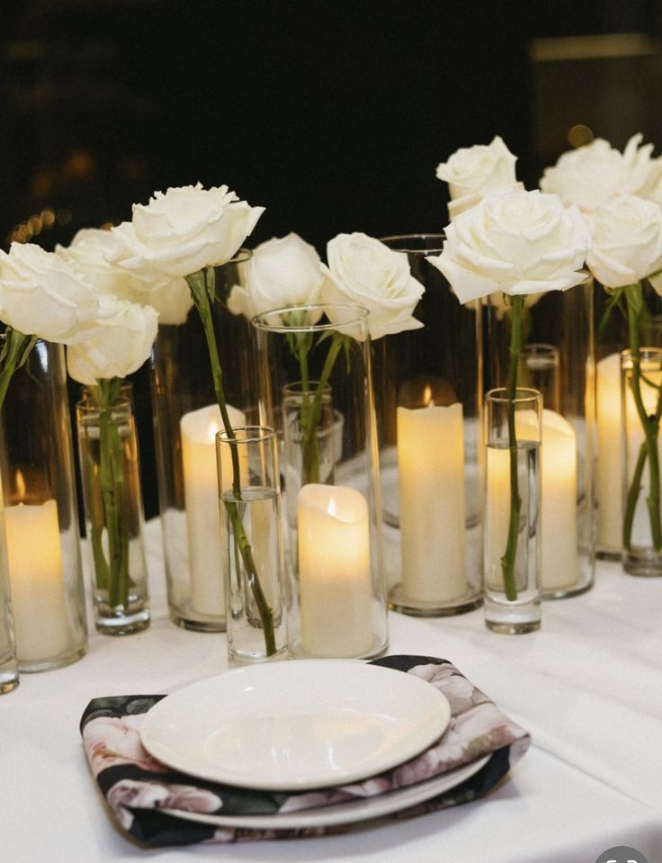 white roses in glass vases and candles on a table set for a formal dinner