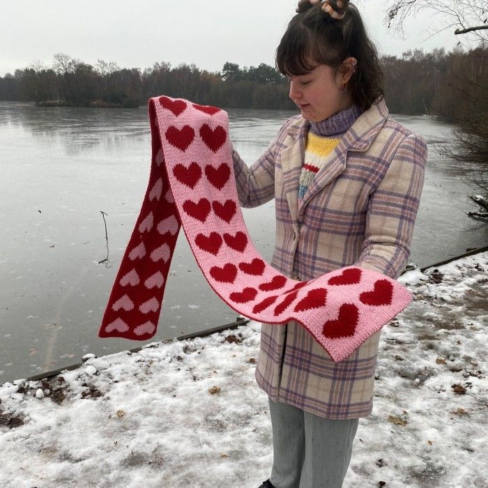 a woman holding up a scarf with hearts on it in the snow near a lake