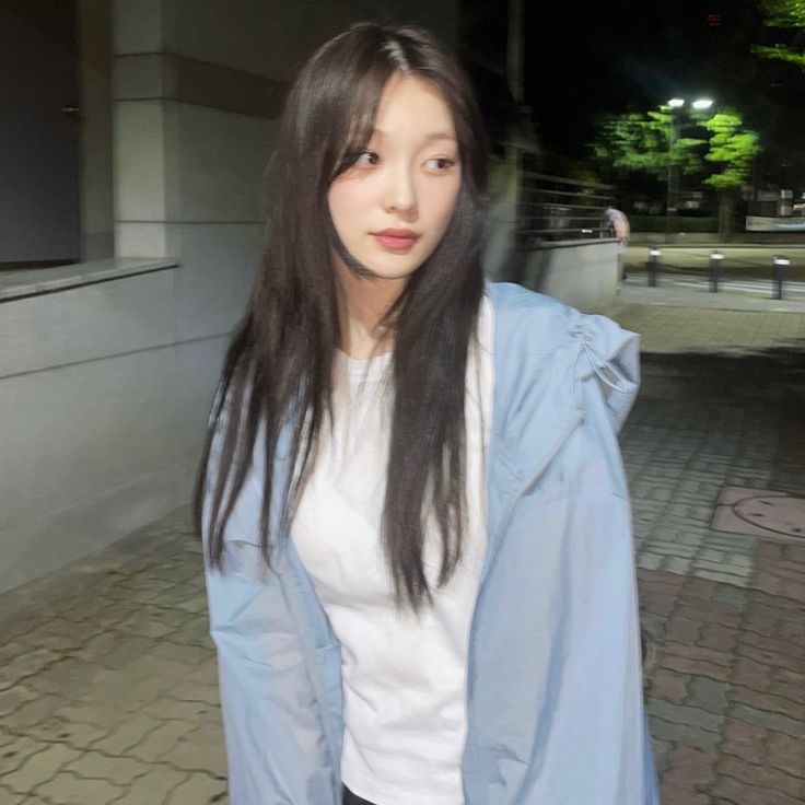 a woman with long black hair wearing a white shirt and blue jacket standing in front of a building