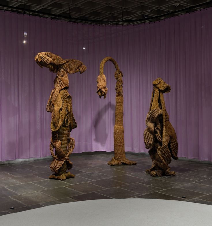 three wooden sculptures are on display in front of a purple curtained wall and floor