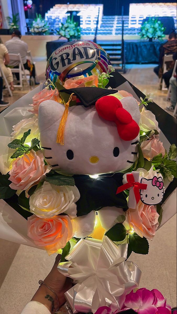 a hello kitty stuffed animal surrounded by roses and other flowers in a room with people