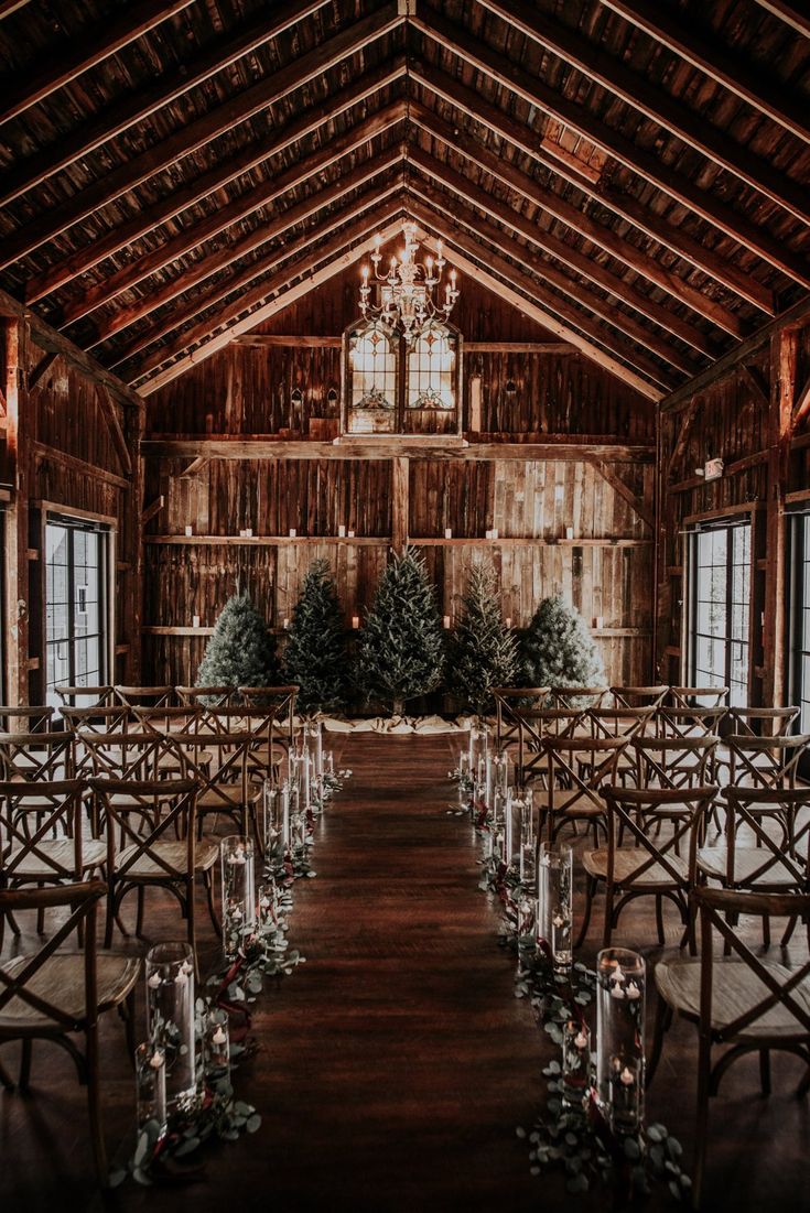 an indoor wedding venue set up with clear chairs and greenery on the aisle, surrounded by candles