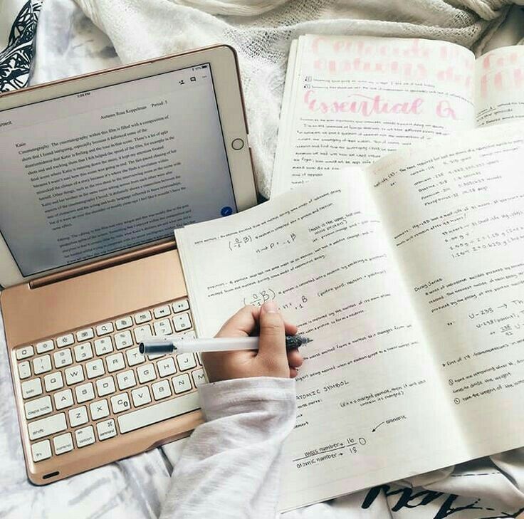 a person is writing on a book and using a laptop with a keyboard next to it