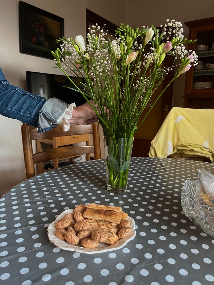 a vase filled with flowers sitting on top of a table next to a plate of cookies