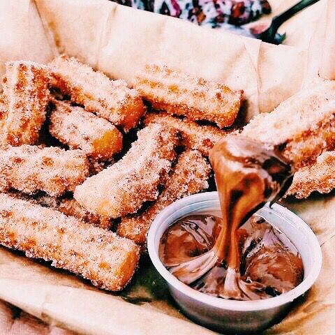 someone is dipping some chocolate into their doughnuts in a basket with other food items