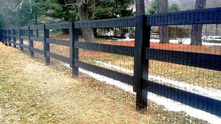 a black metal fence with snow on the ground and trees in the backround