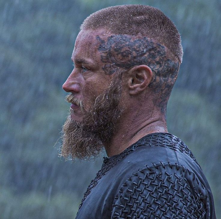 a man with tattoos on his face standing in the rain