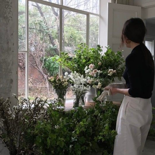 a woman standing in front of a window filled with flowers