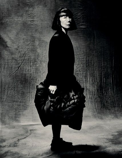 a black and white photo of a woman in a long dress with a bag on her shoulder