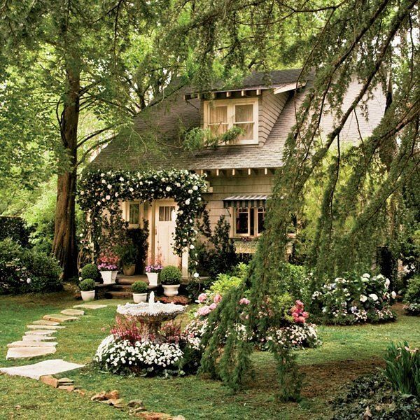 a house with lots of flowers in front of it and trees around the outside area