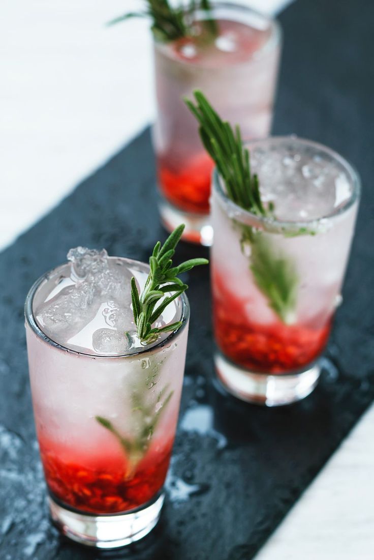 three glasses filled with ice and garnish on top of a black countertop