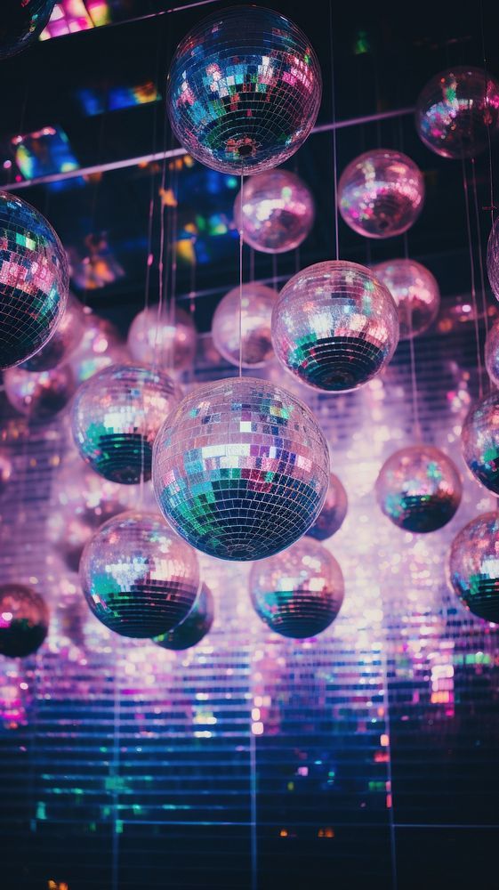 many disco balls hanging from the ceiling in front of a colorful wall with lights on it