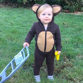 a little boy dressed in a monkey costume holding a banana and standing next to a blue cart