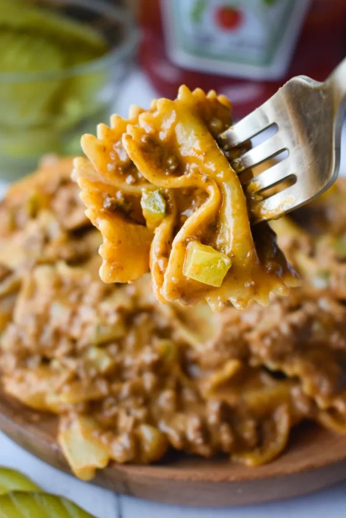 a fork full of pasta with meat sauce and cheese on the plate next to pickles