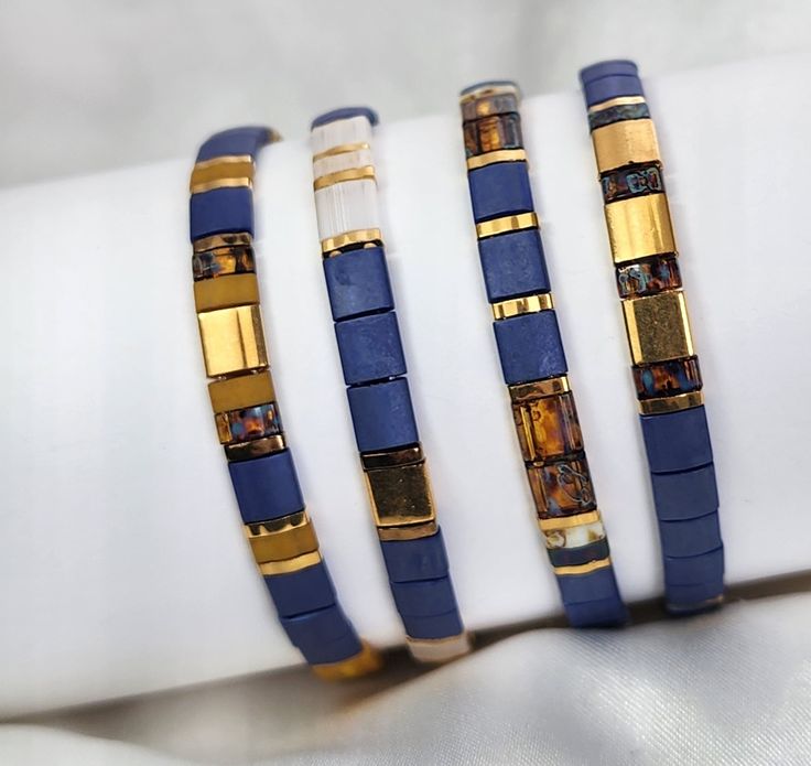 three bracelets with gold and blue beads are on a white napkin, next to each other