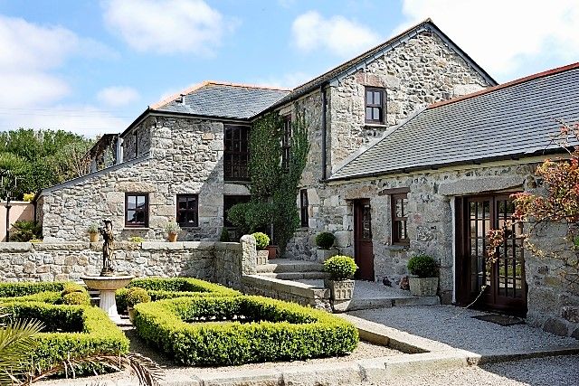 a stone house with hedges in front of it and a water fountain on the side