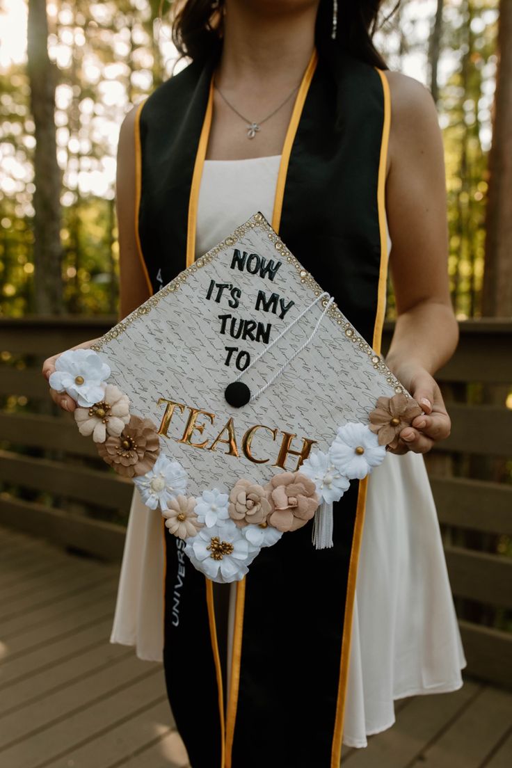 a woman wearing a graduation cap that says now it's my turn to teach