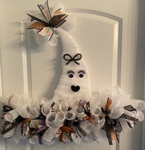 a white door hanger decorated with ribbons and paper mache faces on it's side