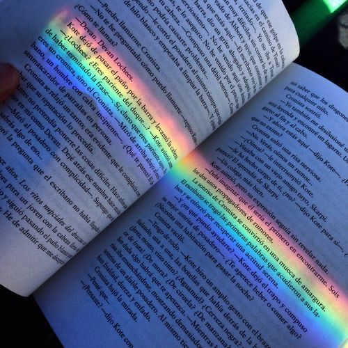 a person is holding an open book with a rainbow light coming out of the book