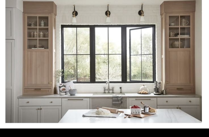 a kitchen with white counter tops and wooden cabinetry next to a large open window