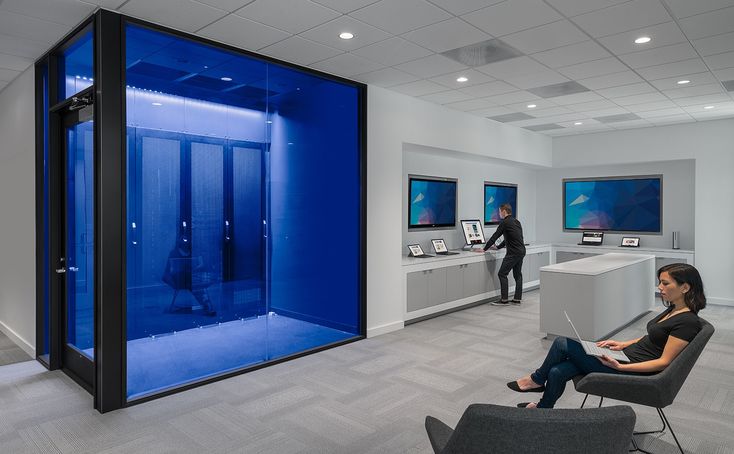 a woman sitting on a chair in front of a blue display case with two women standing behind it