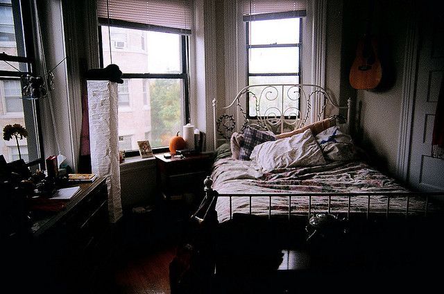 a bed in a bedroom next to two windows with guitars hanging on the wall behind it