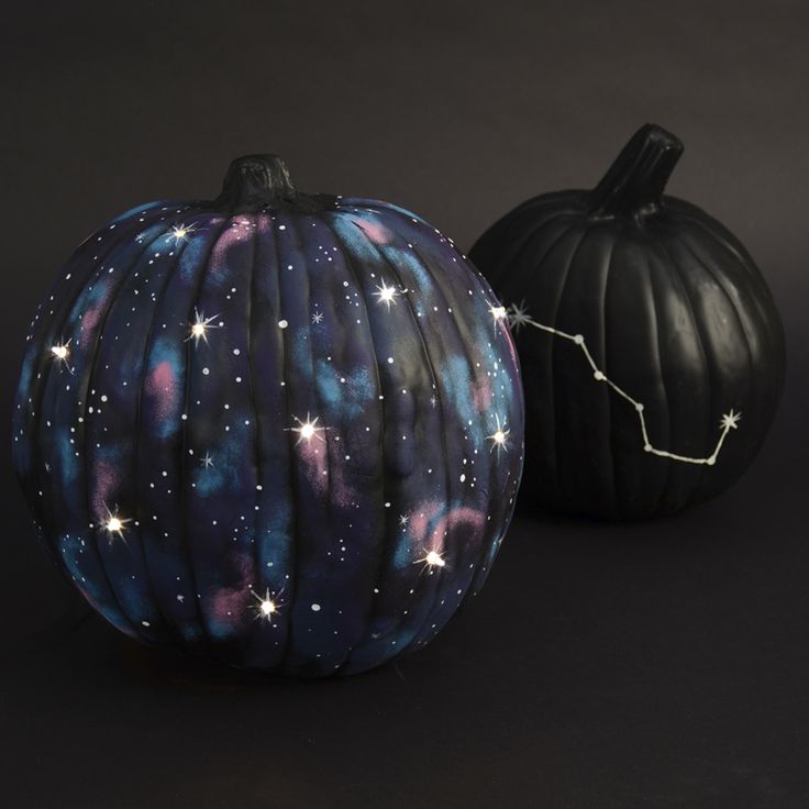 two painted pumpkins sitting next to each other on a black surface with stars in the sky