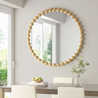 a dining room table with white chairs and a round mirror on the wall above it