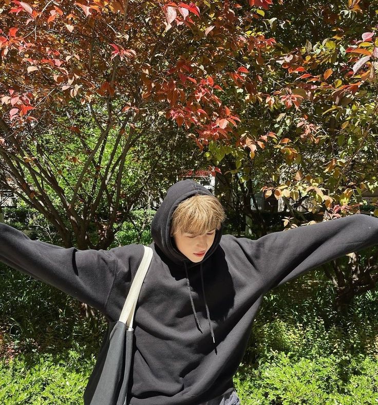 a young man with his arms stretched out in front of a tree and shrubbery