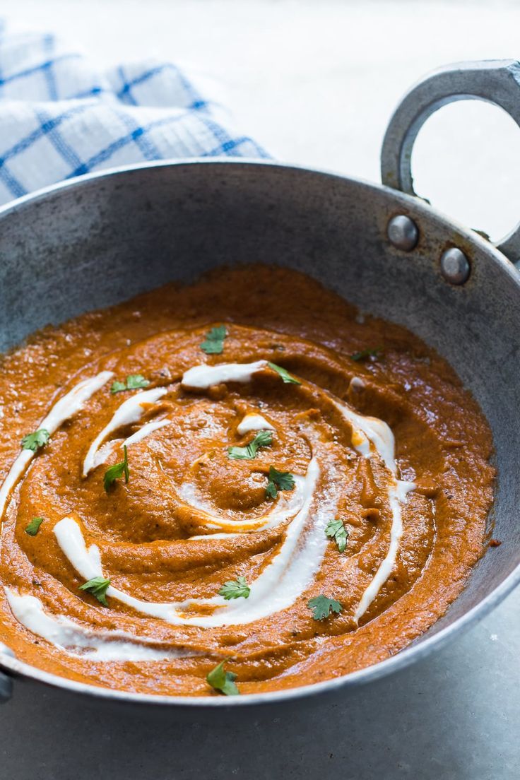 a metal bowl filled with red sauce and garnished with parsley