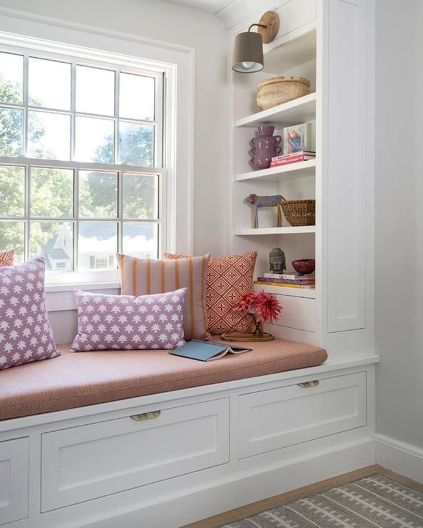 a window seat with pillows on it in front of a book shelf and bookshelf