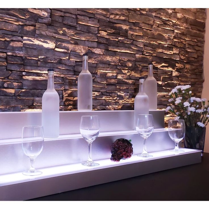 wine glasses and bottles are lined up on a shelf in front of a stone wall