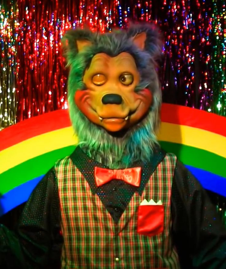 a man in a bear mask and bow tie standing next to a rainbow colored wall