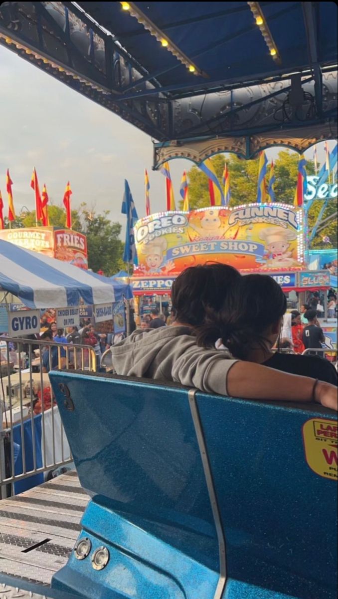 a woman sitting on top of a blue bench in front of an amusement park ride