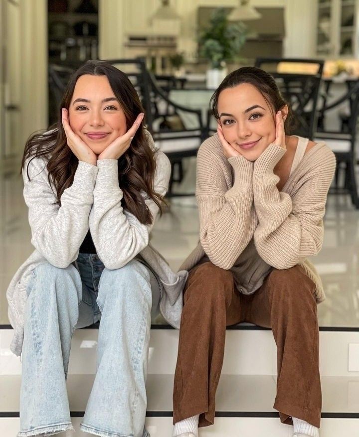 two young women sitting on the floor with their hands behind their heads and looking at the camera